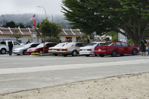 1990 Ford Taurus - Several sedans, including a 1990 Ford Taurus, are parked in a lot on a cloudy day.