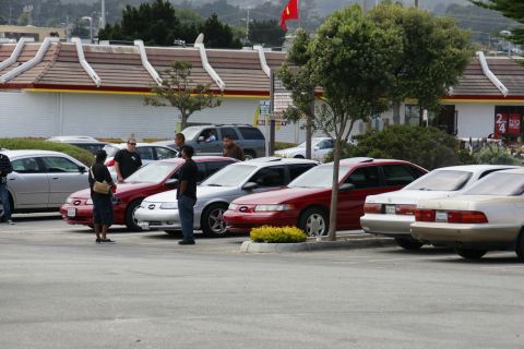 1990 Ford Taurus - A red sedan with a sunroof is parked in a lot with other vehicles.