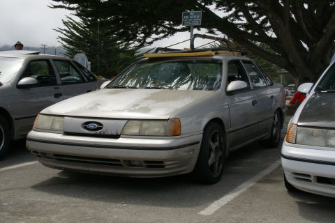 1990 Ford Taurus - Silver 1990 Ford Taurus sedan with a roof rack parked in a lot.