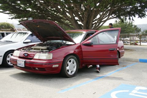 1990 Ford Taurus - A red 1990 Ford Taurus sedan is parked with its hood and driver's door open.