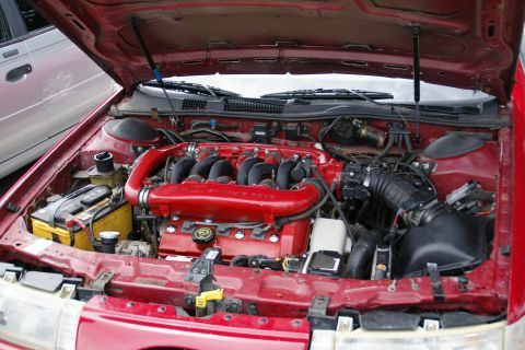 1990 Ford Taurus - Engine bay view of a red V6 engine dual exhaust manifolds and black intake tubes. Text on the intake reads '24 VALVE DOHC'.