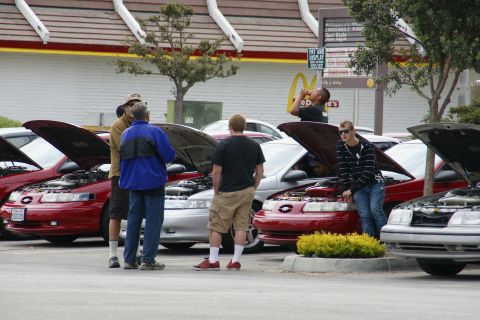 1990 Ford Taurus - People inspect the engines of several Ford Taurus cars parked in a lot.