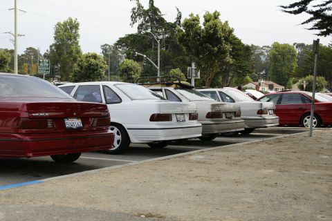 1990 Ford Taurus - Several Ford Taurus sedans are parked in a lot under a cloudy sky.