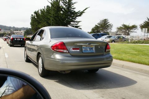 1990 Ford Taurus - A gray Ford Taurus drives in traffic on a sunny day.