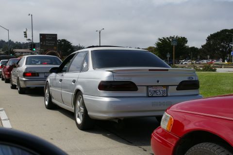 1990 Ford Taurus - A line of cars, including a silver sedan, waits in traffic on a cloudy day.