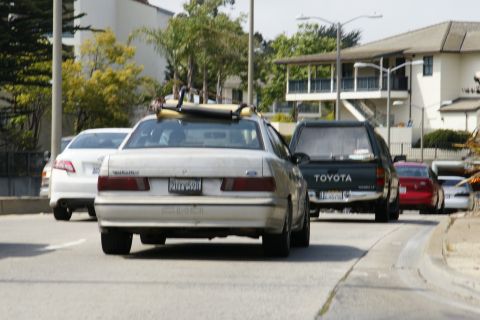 1990 Ford Taurus - A silver 1990 Ford Taurus sedan with a surfboard on its roof rack is seen from behind in traffic.