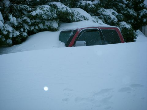 2005 Jeep Wrangler - A red pickup truck is buried in deep snow, with only the top visible above the drifts.