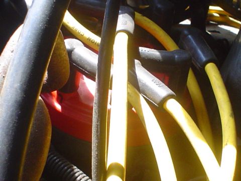 1988 Ford Bronco - Close-up view of yellow spark plug wires and black boots within an engine compartment.