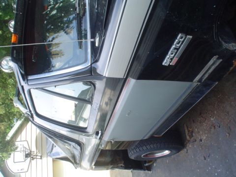 1988 Ford Bronco - The side of a black Ford Bronco is shown, silver body trim and a prominent 'Bronco' emblem.