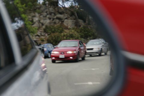 1990 Ford Taurus - A red sedan is seen in traffic, reflected in a side mirror. The vehicle appears to be from the late 1990s.