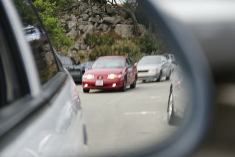 1990 Ford Taurus - A red sedan drives in traffic, reflected in a side mirror.
