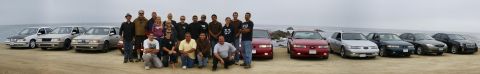 1990 Ford Taurus - A group poses with a collection of 1990 Ford Tauruses on a sandy shore, with the ocean in the background.