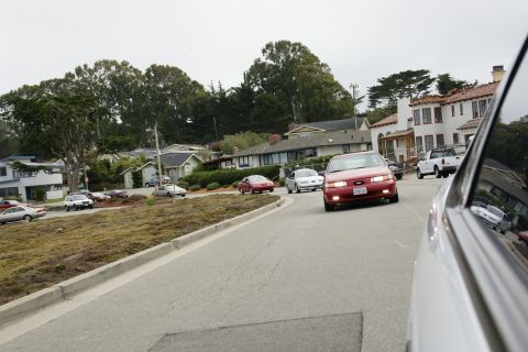 1990 Ford Taurus - A red 1990 Ford Taurus is seen driving on a street in a residential area.
