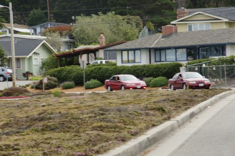 1990 Ford Taurus - Two red sedans are parked in front of houses on a cloudy day.