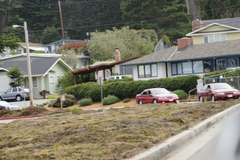 1990 Ford Taurus - Two red sedans are visible in a residential area with houses in the background.