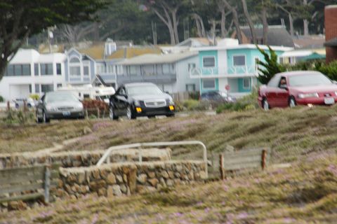 1990 Ford Taurus - A red sedan is seen driving on a road with coastal homes in the background.