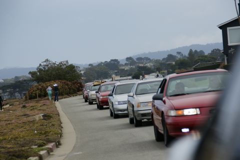 1990 Ford Taurus - A line of cars, including a red 1990 Ford Taurus, drives down a road.