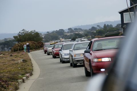 1990 Ford Taurus - A line of cars is seen on a road with a coastal view and houses on the hills.