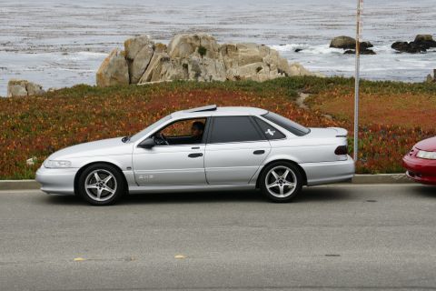 1990 Ford Taurus - Silver 1990 Ford Taurus parked roadside with a red car nearby, ocean in background.