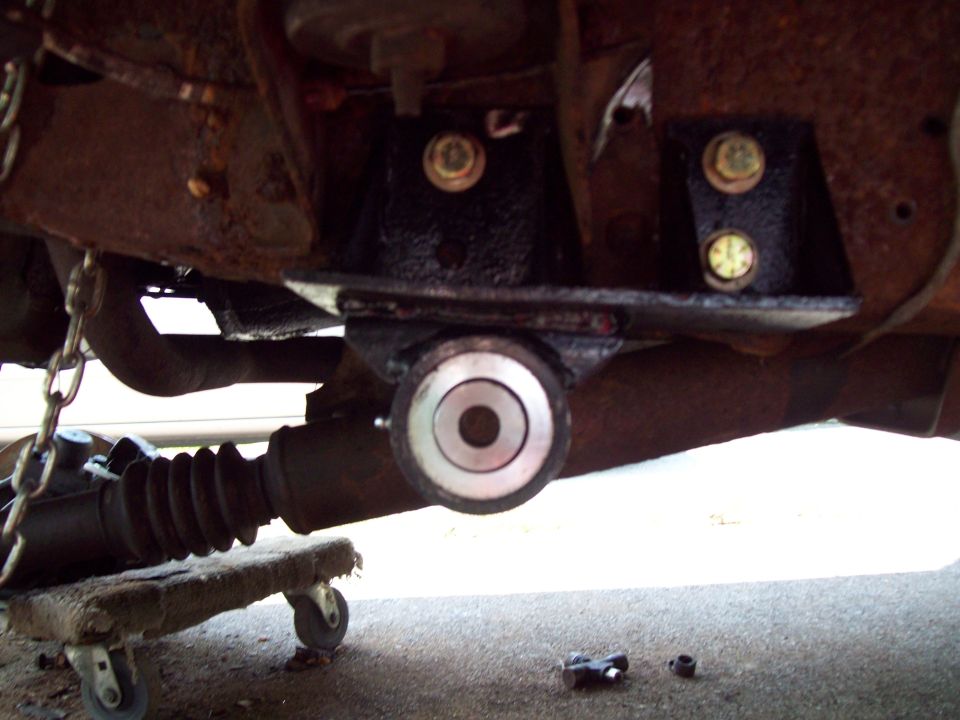 Undercarriage suspension part with rust and new black bracket with yellow bolts