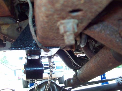 1989 Ford F-150 - Close-up view of a truck's undercarriage, showing suspension components and a chain. A white truck is partially visible in the background.