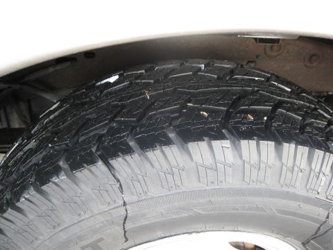 1990 Ford Bronco — Close-up of a worn tire with visible tread damage and debris, showing part of a white vehicle body