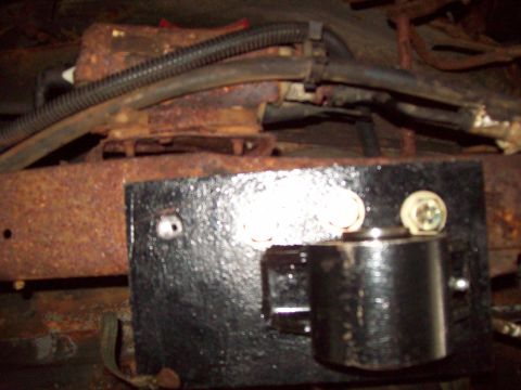 1989 Ford F-150 - The underbody of a vehicle shows significant rust and some newly painted black components, with visible wiring and hoses.