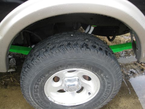 1990 Ford Bronco — Close-up of a vehicle's rear wheel and suspension with green leaf springs