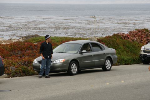 1990 Ford Taurus - Gray Ford Taurus sedan parked on a road with a man standing next to it. Another vehicle is partially visible to the right.