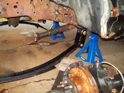 1989 Ford F-150 - Underbody view of a heavily rusted truck frame, showing suspension components and a driveshaft supported by jack stands.