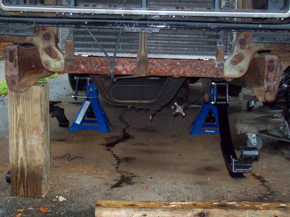 Rusty truck frame on jack stands, showing front suspension and leaf springs