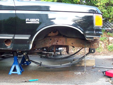 1989 Ford F-150 - The front suspension of a black Ford F-150 is disassembled and supported by jack stands, revealing significant rust on the frame.