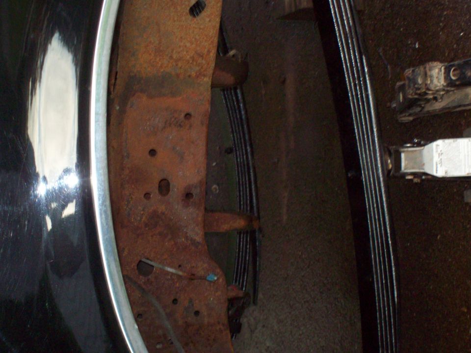 close-up of rusty truck frame with leaf springs and part of a shiny fender