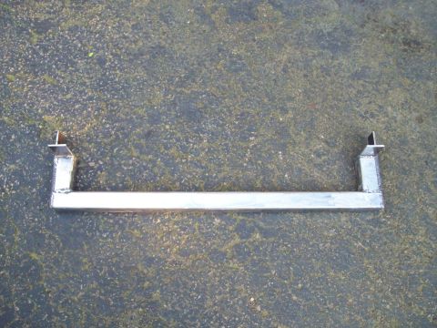 1989 Ford F-150 - A metal bracket is shown lying on a paved surface. The bracket has a long central bar with two angled supports at each end.