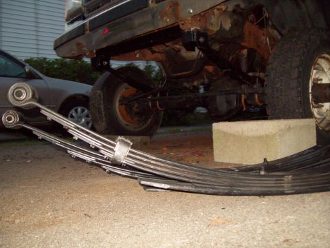 1989 Ford F-150 - The rear axle and leaf springs of a 1989 Ford F-150 are visible, with new leaf springs placed in front of the vehicle.