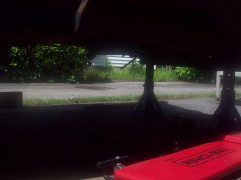 1989 Ford F-150 - The underside of a vehicle is supported by jack stands, with a red creeper visible in the foreground.