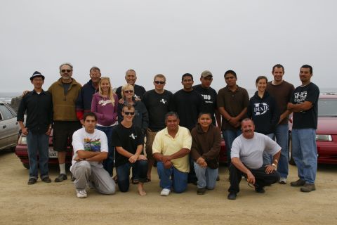 1990 Ford Taurus - A group of people pose for a photo in front of a red sedan on a beach.
