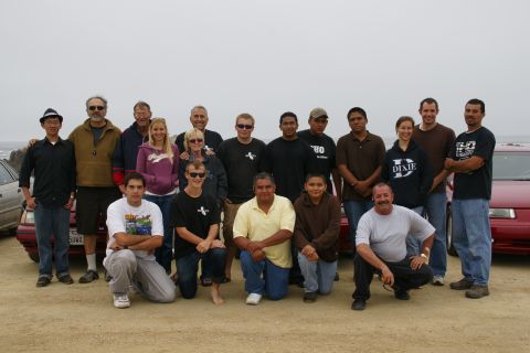 1990 Ford Taurus - A group of people gathered outdoors with several cars visible in the background.