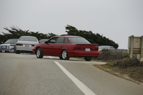 1990 Ford Taurus - A red 1990 Ford Taurus sedan is parked on the side of the road with other vehicles.