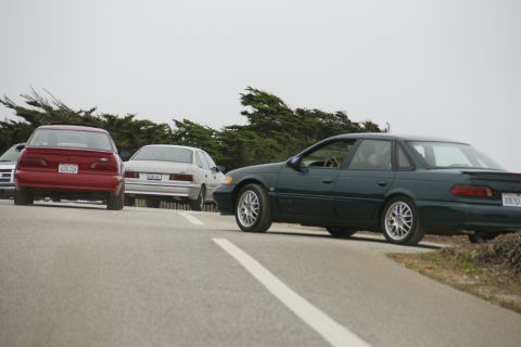 1990 Ford Taurus - A green 1990 Ford Taurus sedan is seen from the side, with other vehicles in the background.
