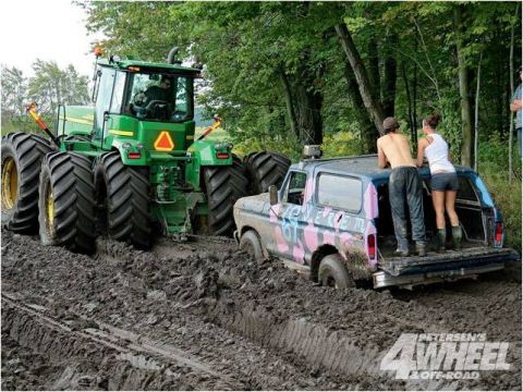 1996 Ford Bronco - A Ford Bronco is stuck in deep mud, with a large tractor attempting to pull it out.