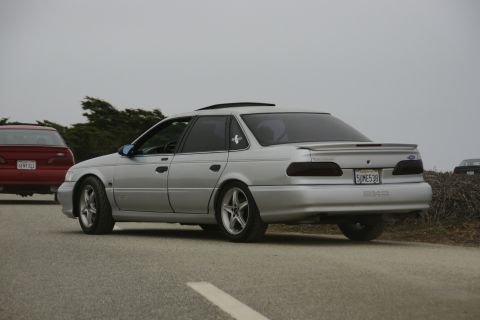 1990 Ford Taurus - Rear view of a silver 1990 Ford Taurus sedan parked on the side of the road with another car to its left.