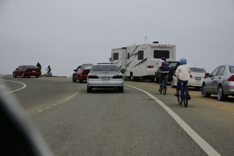 1990 Ford Taurus - Several vehicles are parked along a road, with two people riding bicycles nearby.