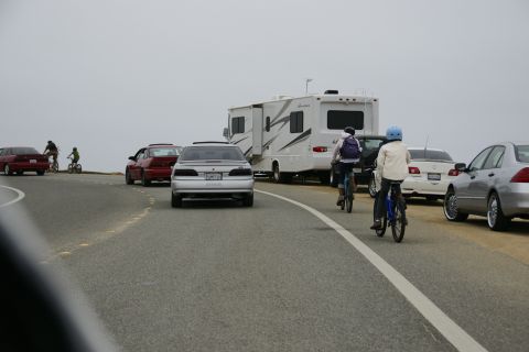 1990 Ford Taurus - Multiple vehicles and cyclists are seen on a road with an overcast sky.