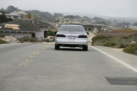 1990 Ford Taurus - Rear view of a 1990 Ford Taurus driving on a road with houses in the background.