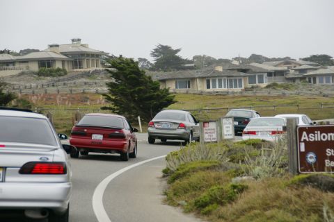 1990 Ford Taurus - Several cars are on a road near coastal homes under an overcast sky.