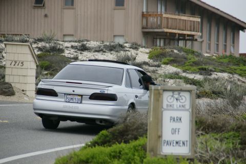 1990 Ford Taurus - A silver 1990 Ford Taurus sedan is seen from the rear on a road next to a sign.