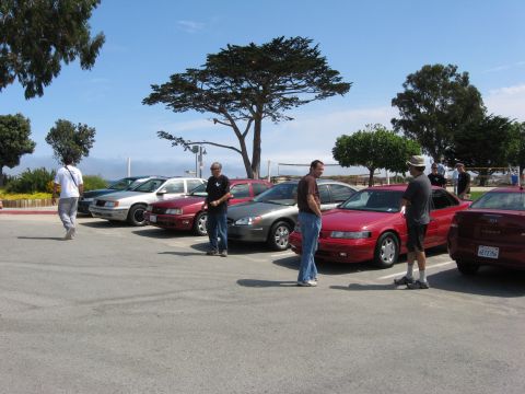 2003 Ford Taurus - People gather around a line of cars parked outdoors on a sunny day.