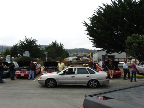 2003 Ford Taurus - A group of car enthusiasts gather around several vehicles, including a silver 2003 Ford Taurus, at an outdoor event.