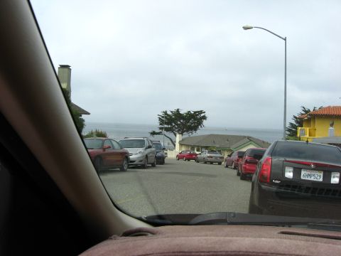 2003 Ford Taurus - A line of cars is parked on a street overlooking the ocean, with a black Cadillac sedan in the foreground.